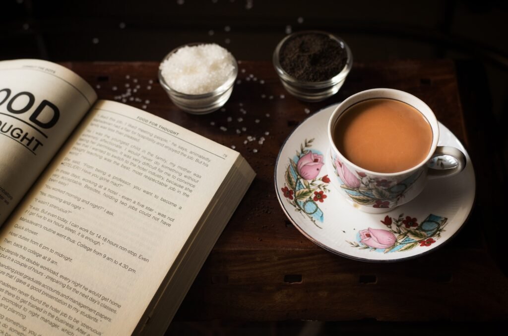 A warm cup of tea, open book, and sugar on a wooden table create a cozy atmosphere.