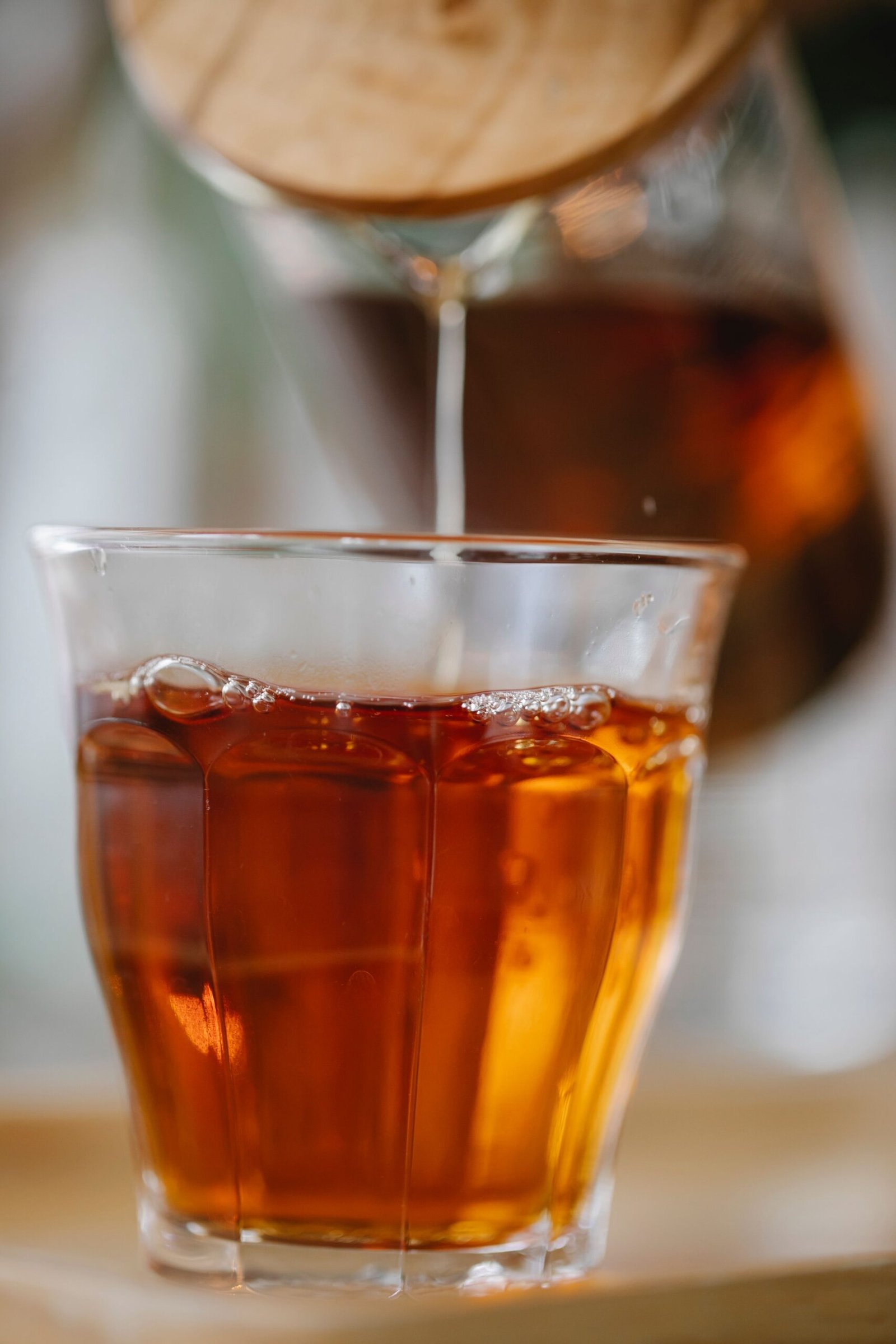 Aromatic freshly brewed black tea pouring from teapot into glass placed on tray